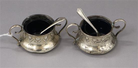 A pair of George V Art Nouveau silver two handled salts and two associated plated spoons.